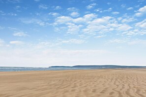 Ein weiter Sandstrand mit sanften Wellen und blauem Himmel.