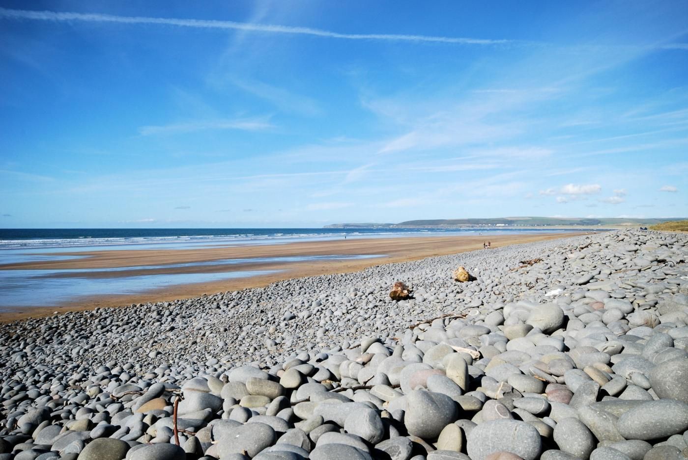 A pebble beach with a view of the sea and distant hills.