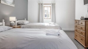 Une chambre avec deux lits, une commode, un téléviseur et une fenêtre avec des rideaux.