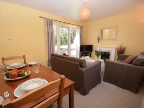 A living room with a sofa, a dining table with plates and cutlery, a television, and a fireplace. - 1 Bed in Braunton (oc-croyd) (Croyde)