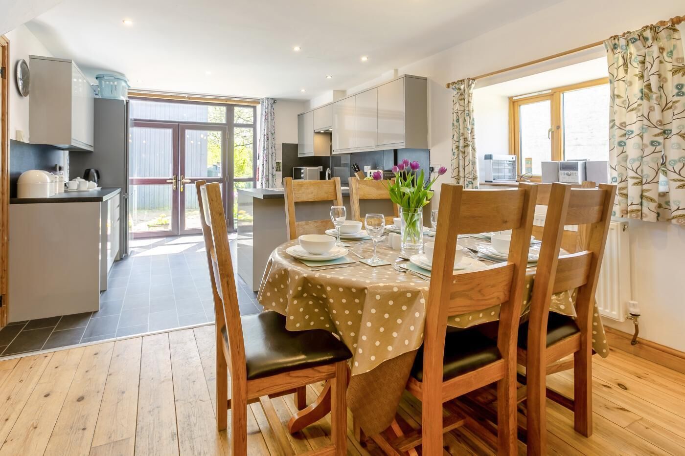A dining area with a round table set for four, wooden chairs, and a view of the kitchen and outside.