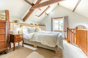 A bedroom with a sloped ceiling, a bed with a patterned bedspread, a wooden dresser, and a window with curtains. - 1 Bed in Beaworthy (oc-00782) (Sheepwash)
