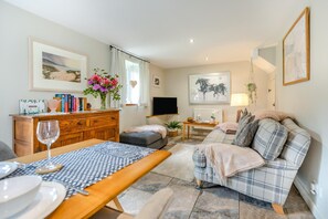 A living room with a wooden table, sofa, and a TV. - 1 Bed in Beaworthy (oc-00782) (Sheepwash)