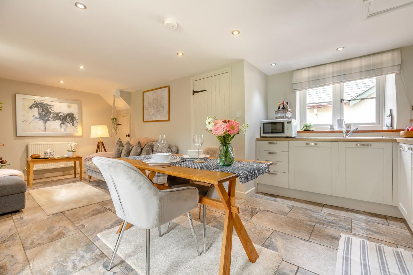 Un coin repas avec une table dressée pour deux personnes, une cuisine avec des meubles blancs et un salon avec un canapé et une lampe.