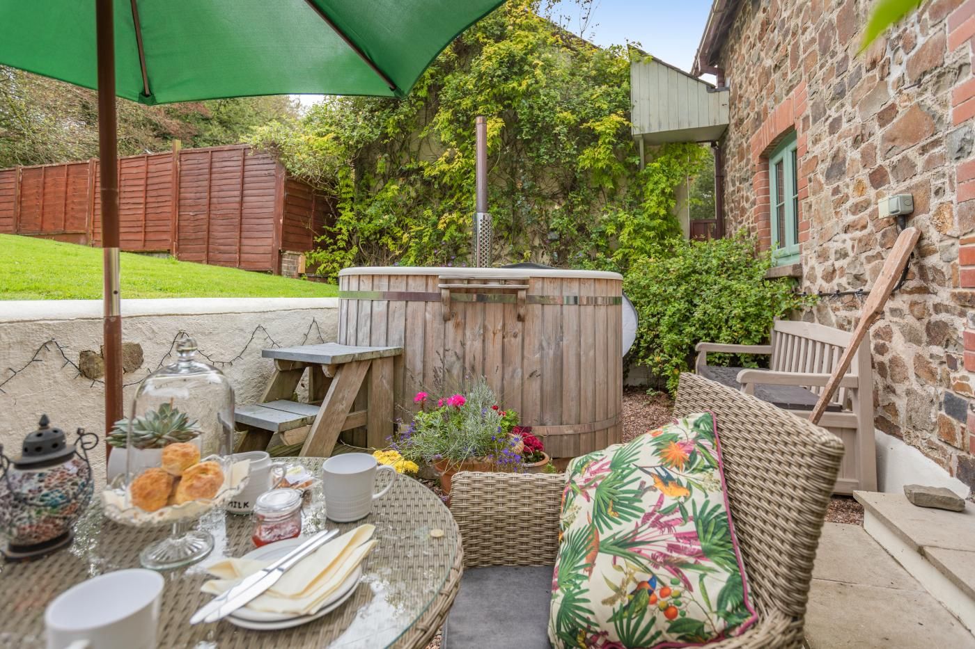 An outdoor patio with a hot tub, wicker furniture, and a table set for dining.