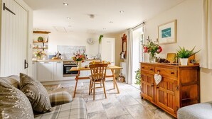Una cocina moderna con armarios blancos, un comedor con una mesa y sillas de madera, y una sala de estar con sofá y un mueble de madera.