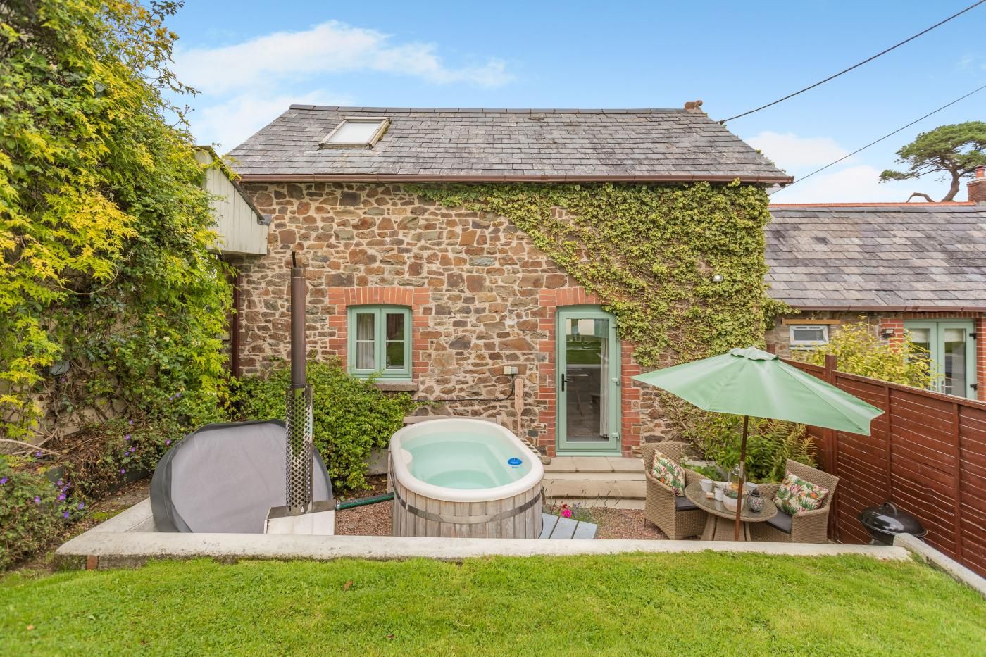 A stone house with a hot tub, a covered patio, and a fenced yard.