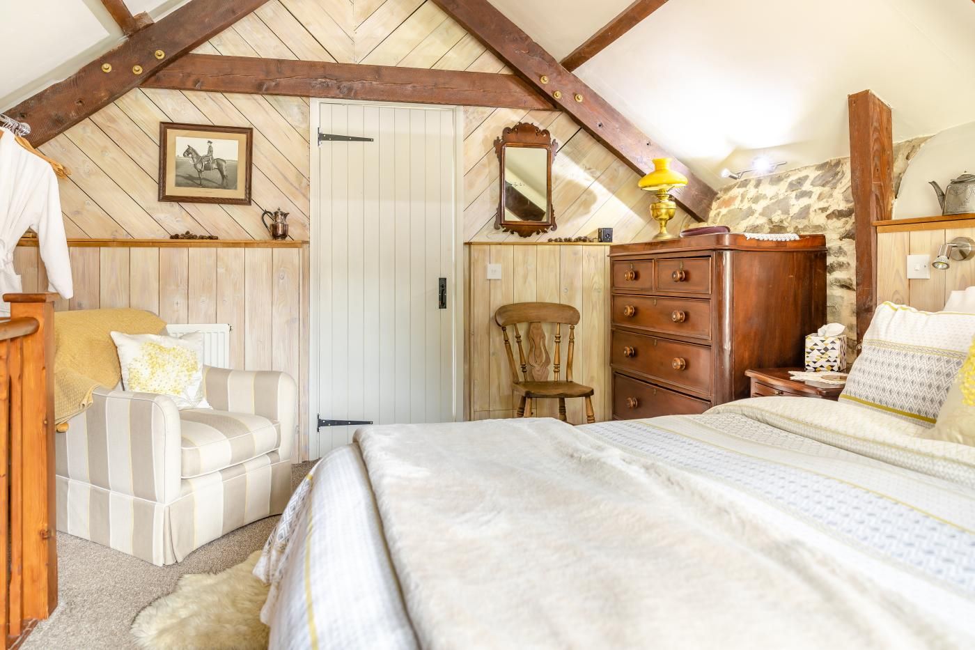 Un dormitorio acogedor con una cama, una silla, un tocador y un espejo.