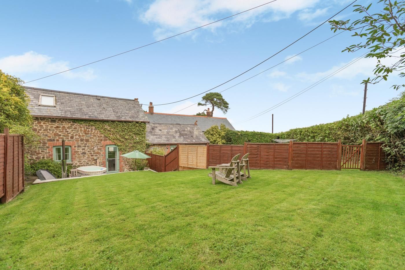 A stone house with a wooden fence, a grassy yard, and a wooden deck with chairs.