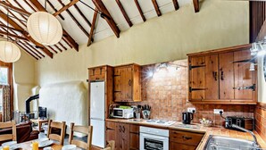 Une cuisine rustique avec des meubles en bois, un dosseret carrelé et un coin repas où une table est dressée pour le petit-déjeuner.