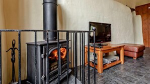 Une pièce avec un poêle à bois noir, un téléviseur posé sur un meuble en bois et un banc en cuir.