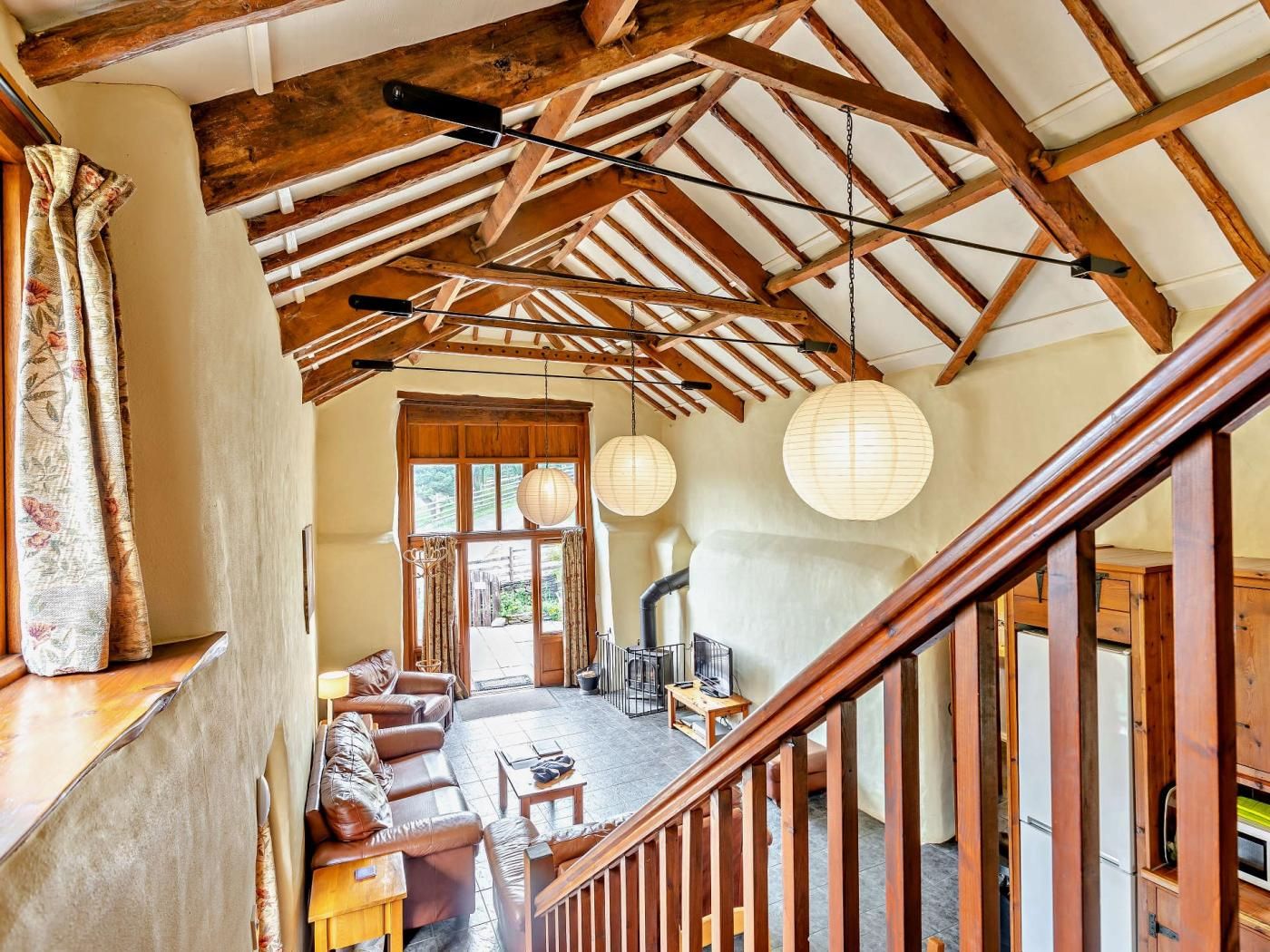 A spacious living area with a high ceiling and exposed wooden beams, a fireplace, and a view through a window.