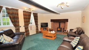 A living room with a fireplace, leather sofas, a wooden coffee table, and a television. - 3 Bed in Exeter (oc-harri) (Talaton)