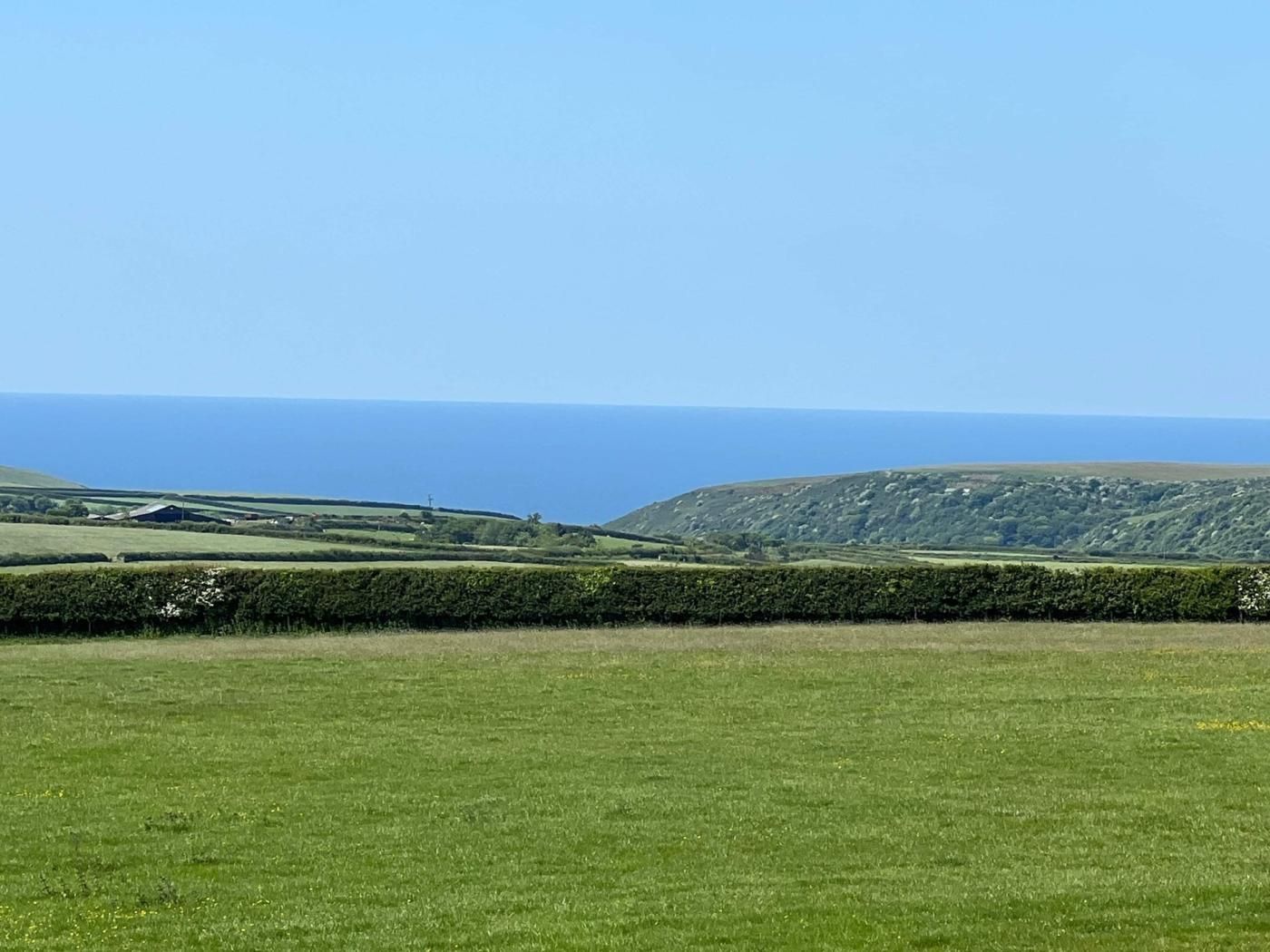 Un champ verdoyant offrant une vue lointaine sur la mer et des collines ondoyantes.