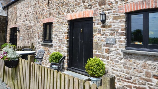 Un edificio in pietra con una porta nera, una piccola finestra e un cartello con su scritto 'FOX BARN'.