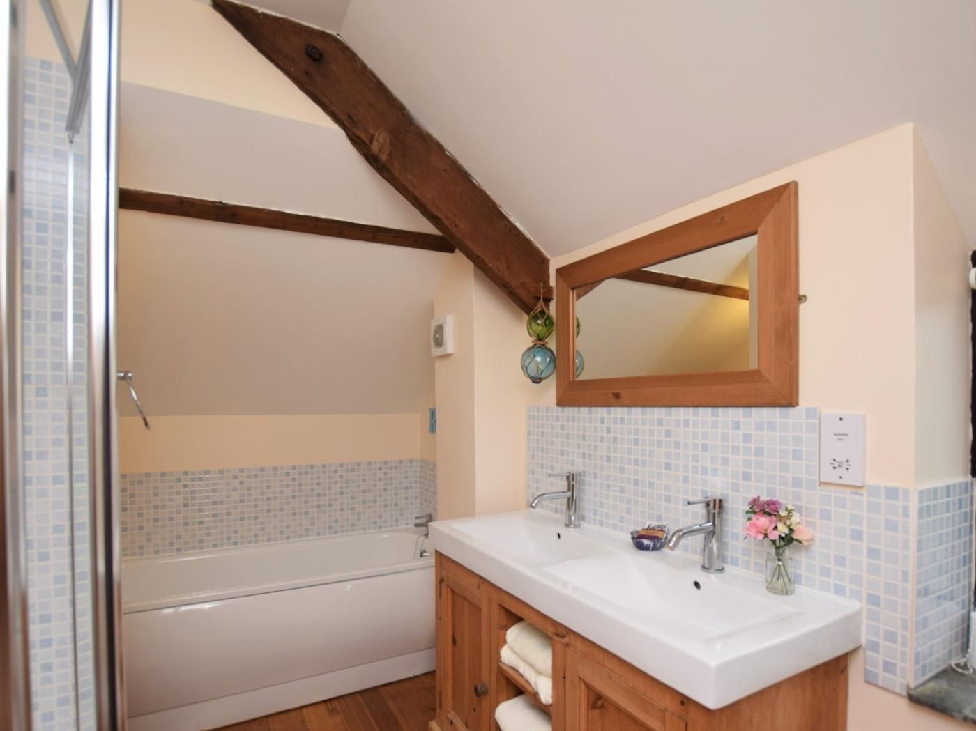 A bathroom with a bathtub, a double sink vanity, and a wooden ceiling beam.