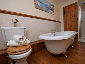 A bathroom with a toilet, a bathtub, wooden flooring, a tiled wall, and a wooden door. - 1 Bed in Beaworthy (oc-hihid) (Shebbear)