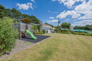 A playground with a slide, a wooden playhouse, and a grassy area. - 2 Bed in Bude (oc-00952) (Launcells)