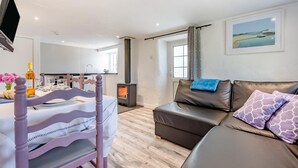 En moderne stue med en sofa, et spisebord dækket til to personer, et fjernsyn ophængt på væggen og en pejs.