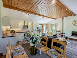 A modern kitchen with wooden ceiling beams, a dining area with a table set for two, and a living room with a sofa and a fireplace. - 2 Bed in South Molton (oc-islvi) (South Molton)