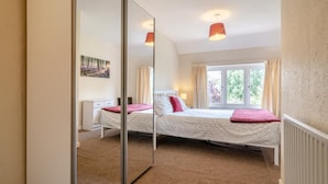 A bedroom with a bed, a nightstand, a mirror, a window with curtains, and a painting on the wall.