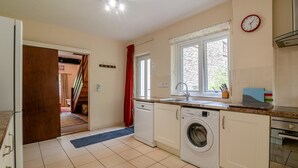 A kitchen with a washing machine, a sink, a window, and a clock on the wall.
