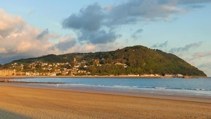 A coastal town with buildings on a hill, a beach, and a clear sky.