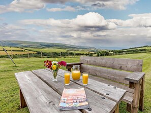 Ein Holztisch für ein Picknick, mit einer Zeitschrift, einem Blumenstrauß und zwei Gläsern Orangensaft.