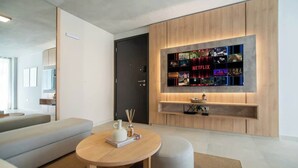 A modern living room with a flat-screen TV mounted on a wooden wall, a sofa, a round coffee table, and a door. - Corporate Stays Insignia City - B52 (Asunción)