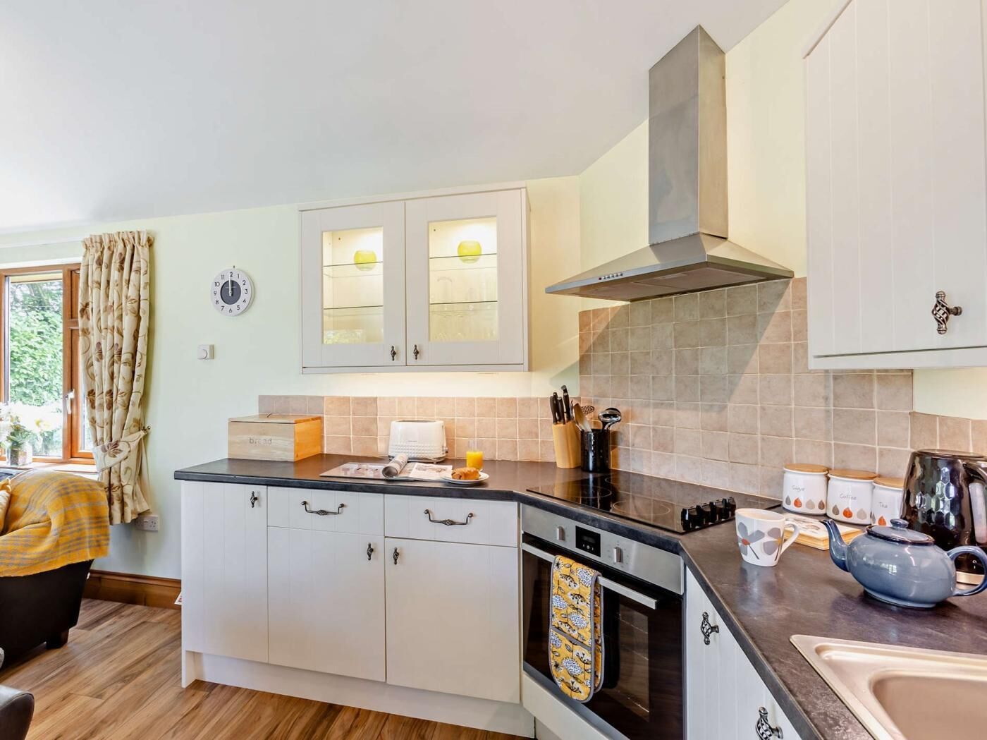 A kitchen with white cabinets, a stainless steel range hood, a built-in oven, and a window with curtains.