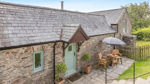 A stone cottage with a tiled roof, a green door, and a patio with a table and chairs. - 1 Bed in Taunton (oc-oldli) (Wiveliscombe)