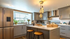 Cocina moderna con armarios grises, una isla central con taburetes, un extractor de acero inoxidable y una ventana con persianas.