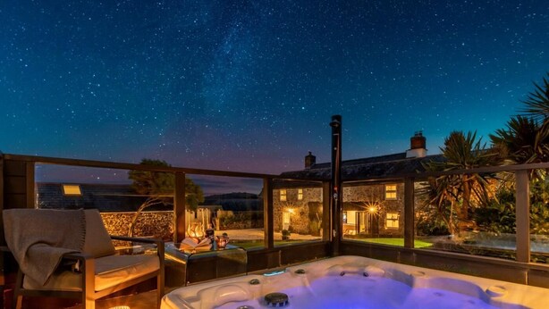 Jacuzzi con vista a un cielo estrellado, terraza de madera y pared de piedra.