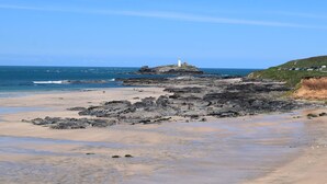 A coastal landscape with a lighthouse on a rocky outcrop, a sandy beach, and a grassy hill in the background. - 2 Bed in Camborne (oc-oldmm) (Camborne)