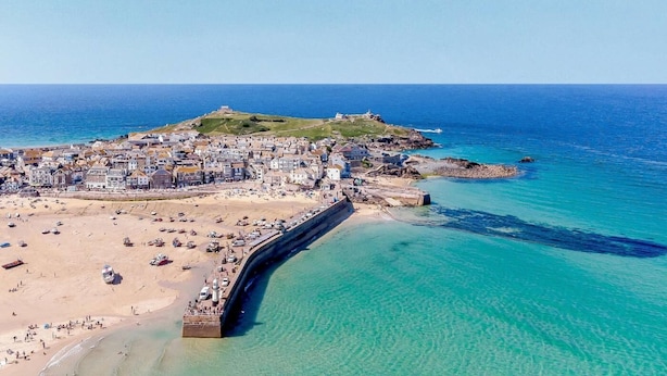 Une ville côtière dotée d’une plage, d’une jetée et d’une forteresse située sur une colline.