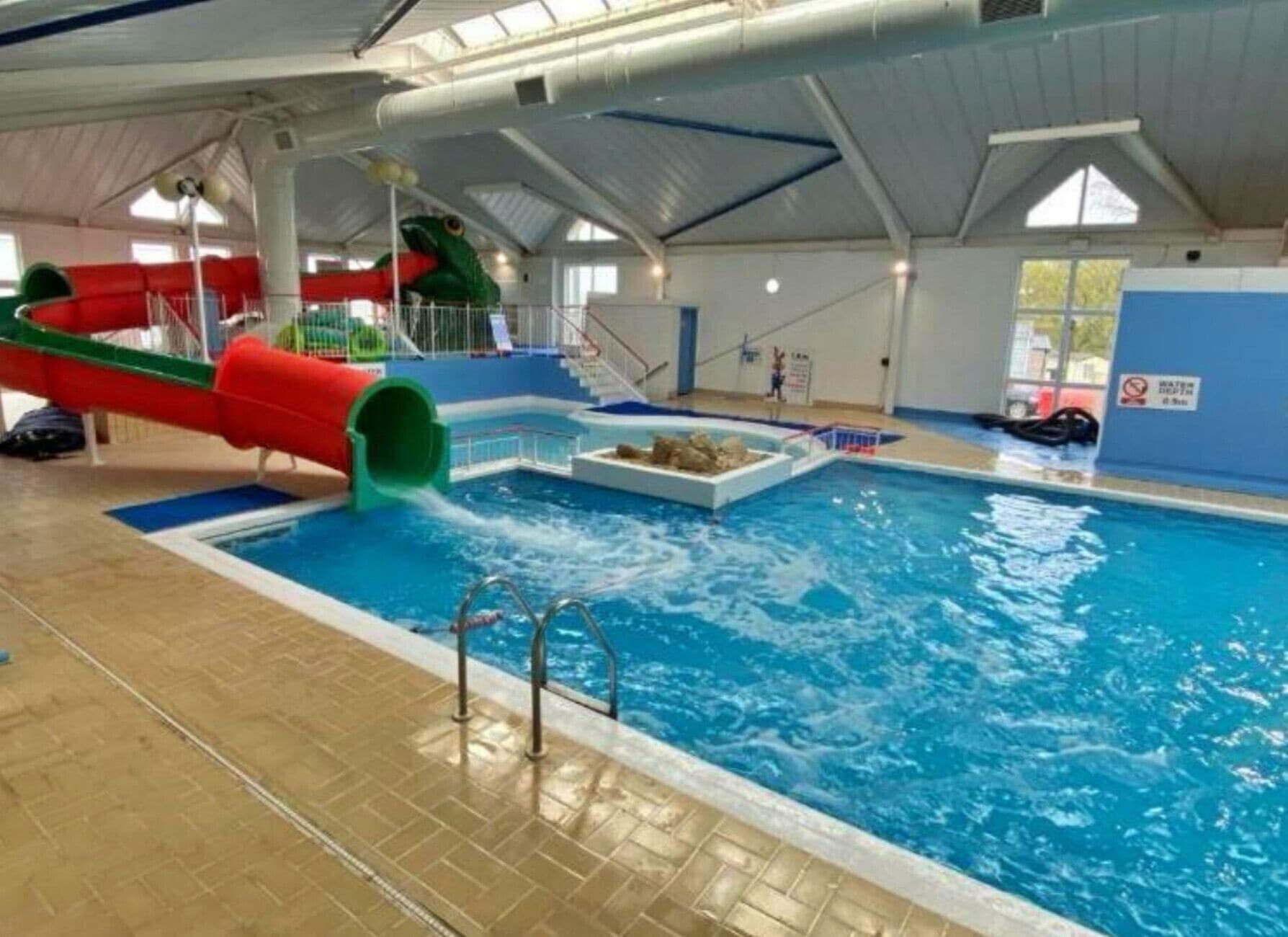 An indoor swimming pool with a slide, a diving board, and a lifeguard stand.