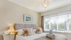 A bedroom with a bed, a nightstand, a lamp, a window with blinds, and a chandelier. - 2 Bed in Barnstaple (oc-oldma) (Landkey)