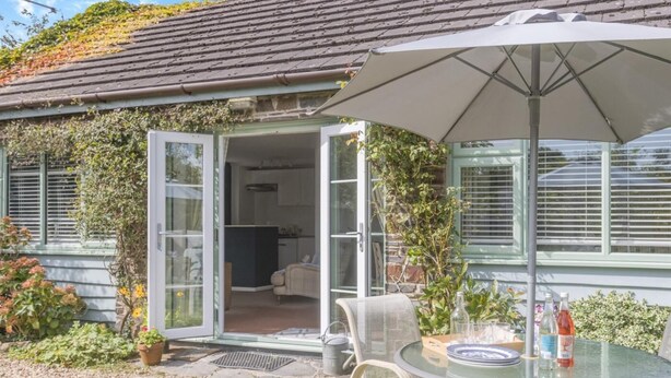 A glass-enclosed patio with a table and chairs, a white umbrella, and a view of the interior. - 2 Bed in Barnstaple (oc-oldma) (Landkey)