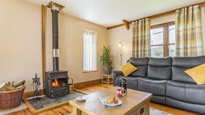 A cozy living room with a fireplace, a sofa, a coffee table with croissants, and a window with curtains. - 3 Bed in Callington (oc-mbarn) (Linkinhorne)
