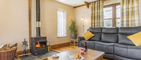A cozy living room with a fireplace, a sofa, a coffee table with croissants, and a window with curtains.