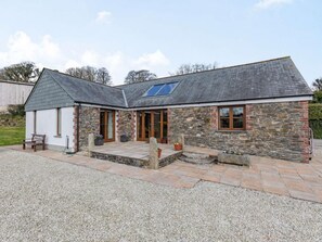 A stone house with a sloped roof, a patio area with seating, and a small garden. - 3 Bed in Callington (oc-mbarn) (Linkinhorne)
