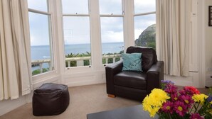 A room with a view of the sea, a leather sofa, a small ottoman, and a vase of flowers. - 2 Bed in Ilfracombe (oc-oedge) (Ilfracombe)