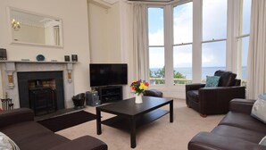 A living room with a fireplace, a flat-screen TV, a coffee table, and a sofa. - 2 Bed in Ilfracombe (oc-oedge) (Ilfracombe)