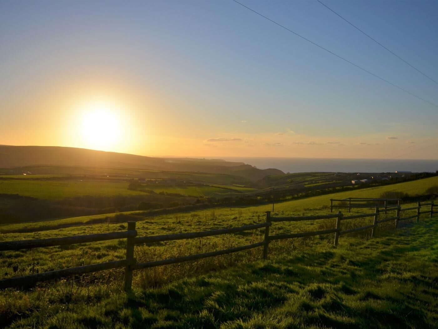 A rural landscape with rolling hills, a wooden fence, and a clear sky.