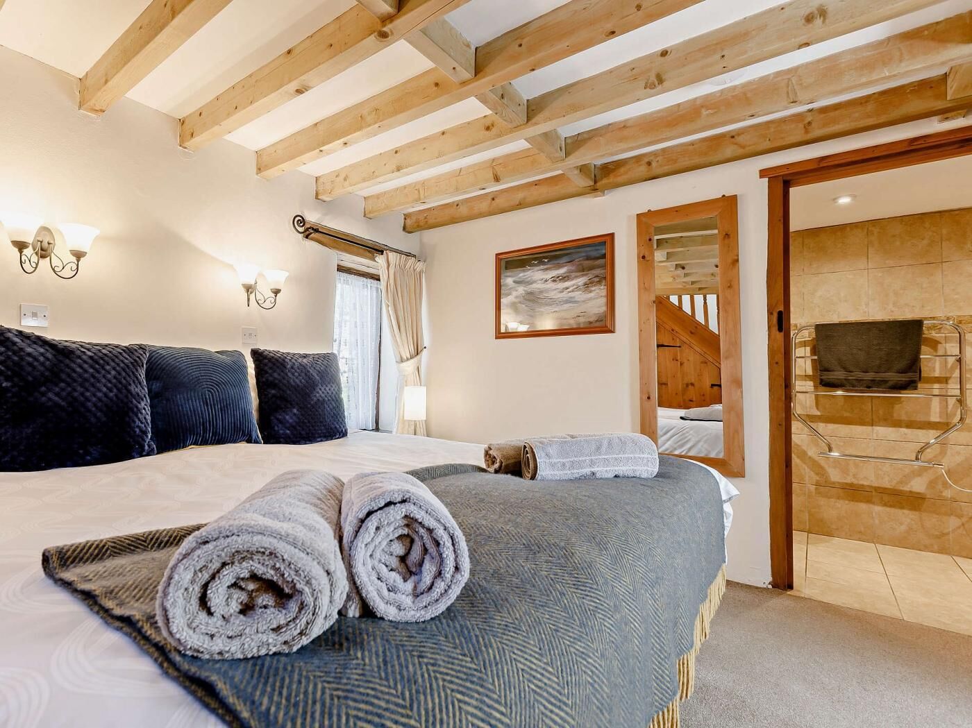 A hotel room with a bed, towels, a painting, a TV, and a wooden staircase.