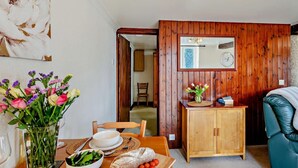 Ein Essbereich mit Holztisch, Stühlen, einer Blumenvase, einer Salatschüssel, einem Brotlaib und einem Holzschrank.