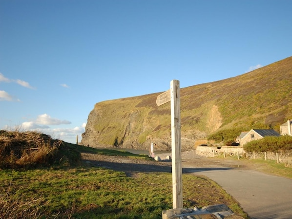 A rural road with a wooden signpost, a stone building, and a grassy area. - 1 Bed in Nr Bude (oc-penke) (Crackington)