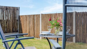 Un espace patio avec une table dressée pour deux personnes, une chaise et un vase décoratif rempli de fleurs.