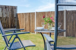 A patio area with a table set for two, a chair, and a decorative vase with flowers. - 1 Bed in Nr Bude (oc-penke) (Crackington)