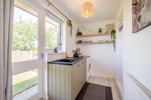A narrow kitchen with a window, a sink, a washing machine, and a hanging light fixture. - 1 Bed in Nr Bude (oc-penke) (Crackington)